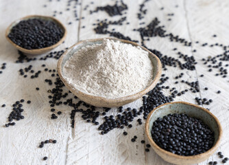Bowls with  black lentils flour and beans on white wooden table close up