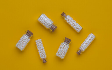 Homeopathic globules in small glass bottles on a yellow background. Alternative treatment.