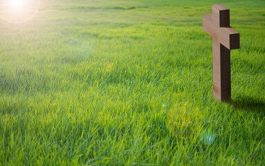 Kreuz aus Holz steht auf einer grünen Wiese. Die Sonne scheint stimmungsvoll auf das Kreuz. Ostern, viel Platz für Text, copy space.