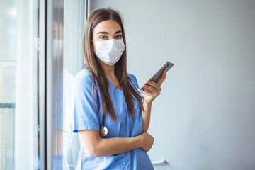 Shot of a masked young doctor using a smartphone. Sad modern physician woman using phone app....