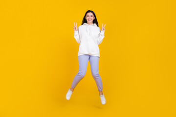 Fototapeta na wymiar Full length photo of autumn youngster lady jumping make v-sign isolated over shine yellow color background