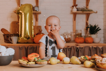 smiling one-year-old baby boy in festive clothes holds an apple in his hands. first birthday. body with the number one. golden foil ball. healthy snack for kids. little chef. High quality photo