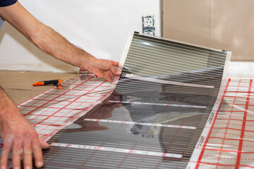 a man lays down a strip of infrared floor heating. Building materials. Repair. 