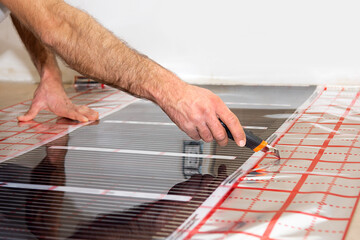 a man cuts a strip of infrared floor heating. DIY repair. Cutting of building materials. Film floor
