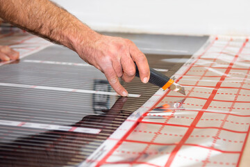 a man cuts a strip of infrared floor heating. DIY repair. Cutting of building materials.