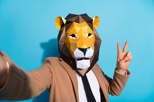 Portrait of weird incognito guy lion mask take selfie video call unusual occasion make v-sign isolated over blue color background