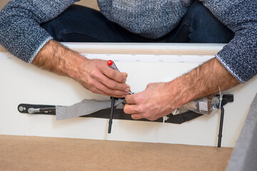 Hands screwing the lifting mechanism to the bed. Assembling furniture yourself at home. 