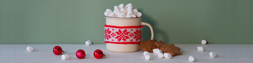 Bunner Marshmallows fall like snow into a cozy cup with New Year's knitted decoration. The concept of a Christmas dinner while waiting for Santa Claus. Cocoa and biscuits, red and white decor.
