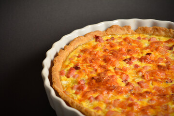 Close up of whole traditional French pie quiche Lorraine with ham, onion and eggs. Backed custard dough served on plate. Classic recipe. Black background.
