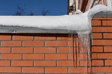 Icicles are hanging from the eaves of the building,covered with a thick snow layer. Danger from falling icicles and snow