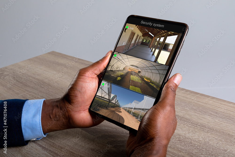 Poster hands of caucasian man holding smartphone with views of farm from security cameras on screen