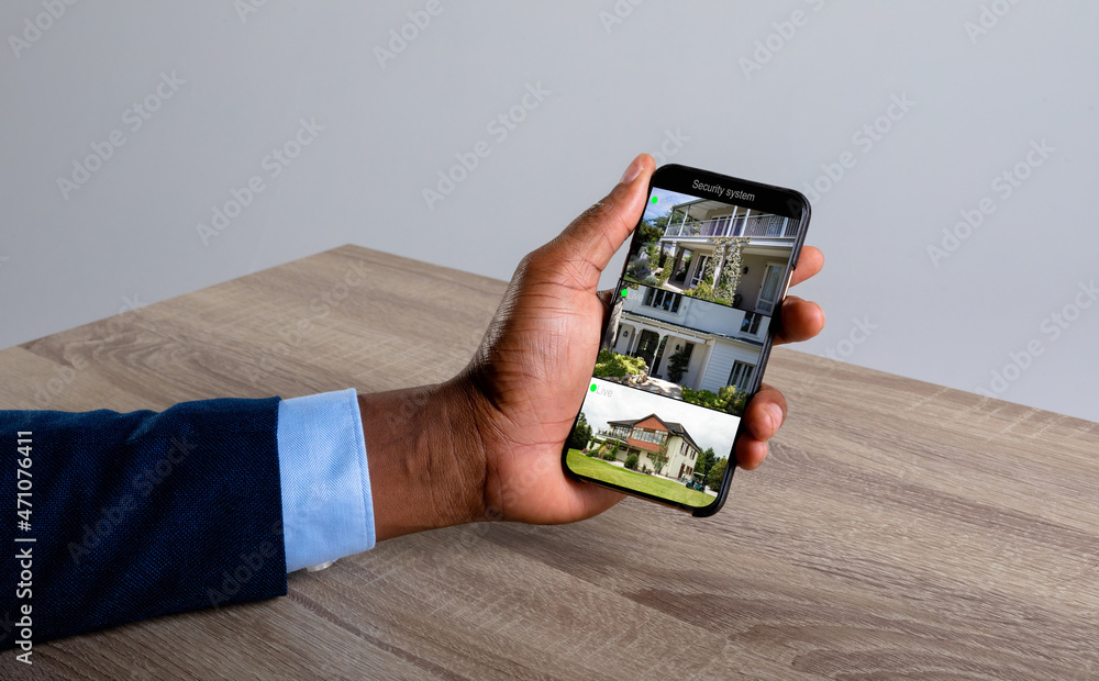 Canvas Prints Hand of caucasian man holding smartphone with views of home from security cameras on screen