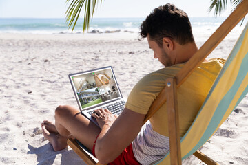 Caucasian man on holidays using laptop with views of home from security cameras on screen