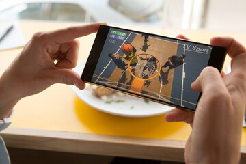 Hands of caucasian man at restaurant watching basketball on smartphone