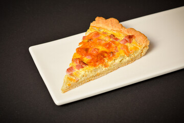 Side view of piece of pie with onion, eggs and bacon. French traditional quiche Lorraine. Baked Custard dough. Close up of Pie slice on white plate on black background
