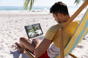 Caucasian man on holidays using laptop with views of home from security cameras on screen