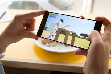 Hands of caucasian man at restaurant watching smartphone with baseball match on screen