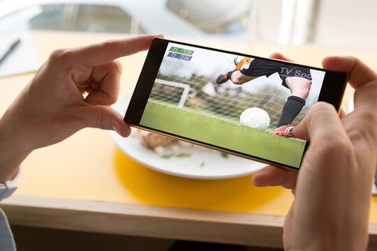 Hands of caucasian man at restaurant watching soccer match on smartphone