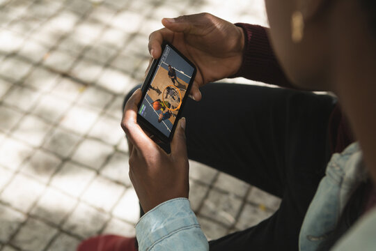African american man in park watching basketball match on smartphone