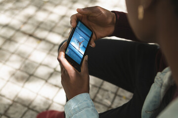 African american man in park watching swimming competition on smartphone