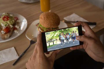 Hands of caucasian man at restaurant watching marathon runners on smartphone