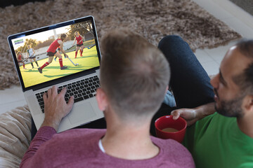 Two diverse male friends at home watching hockey match on laptop - Powered by Adobe