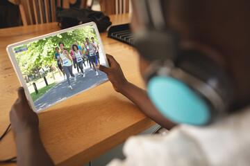 African american boy wearing headphones at home watching marathon on tablet