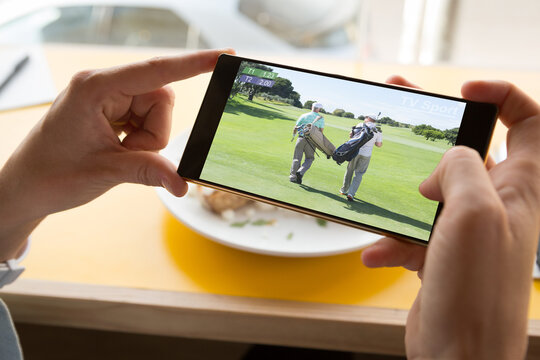 Hands of caucasian man at restaurant watching golf match on smartphone