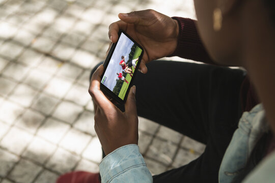 African american man in park watching rugby match on smartphone