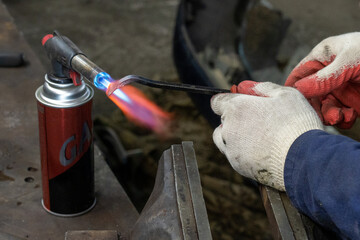 Naklejka premium Photo of a gas burner and metal melting. Male hands in work gloves in the garage