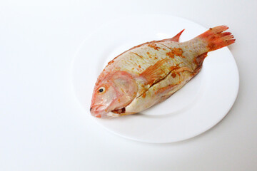Red Nile Tilapia, or Red Tilapia, or Oreochromis niloticus. Fresh fish seasoned with mashed turmeric. On a plate, isolated on white background