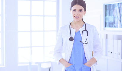 Female doctor standing with stethoscope and her hands in pockets at hospital