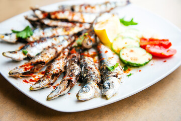 Fresh Grilled sardines served with fresh tomatoes, cucumbers slices and lemon on white plate for mediterranean healthy meal