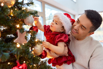 winter holidays and family concept - happy middle-aged father and baby daughter decorating christmas tree at home