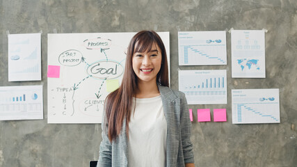 Fototapeta premium Portrait of successful beautiful executive businesswoman smart casual wear looking at camera and smile, happy in modern office workplace. Young Asia lady stand relax in contemporary coworking space.
