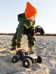 Boy kid playing radio control car riding on sand outdoor enjoying happy childhood