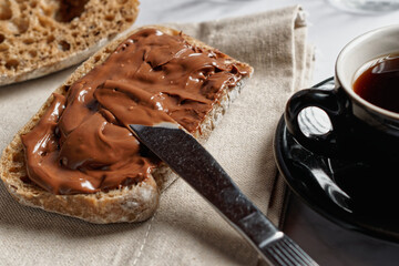 Chocolate spread on halved rye roll, next to a cup of coffee