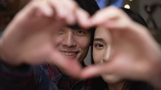 Happy young couple in love showing heart with their fingers and face camera smiling. cheerful girl and boyfriend looking at lens close up view smiling with love gesture on hands