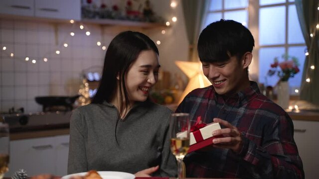 Handsome asian young man making unexpected surprise present for beautiful and charming girlfriend at date night at home. guy closing girl eyes with hands and sending gift on valentines day.