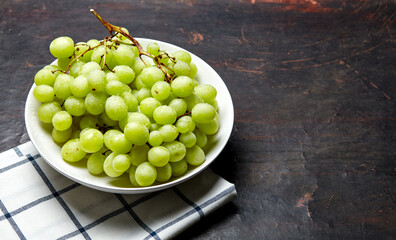 Branch of ripe green grape on plate with water drops. Juicy grapes on wooden background, closeup. Grapes on dark kitchen table with copy space