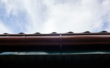 Fototapeta premium Facade of a suburban building with downspout. View of the roof against the sky