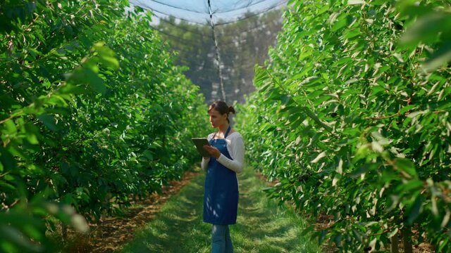 Woman farmer collecting data with modern device in green plantation smiling