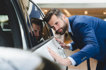 Young successful caucasian businessman checking new car options at dealer shop before buying it,...