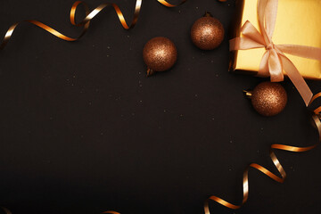 Christmas or New Year decoration - golden gift, Christmas baubles and serpentine over black background. Greeting card. Copy space.