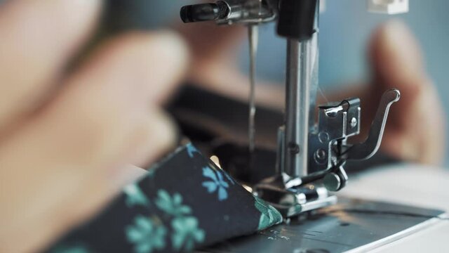Women's hands raise foot of sewing machine and pull fabric by threads in wrong direction. Malfunctions and stopping of mechanism in sewing machine. Dressmaker's workshop.