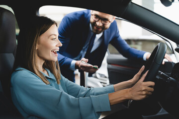 Satisfied happy caucasian female client customer woman sitting at the wheel of new car doing...