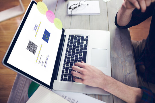 Caucasian man sitting at desk using laptop with covid vaccination certificate and qr code on screen