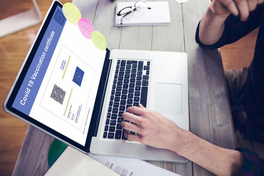 Caucasian man sitting at desk using laptop with covid vaccination certificate and qr code on screen