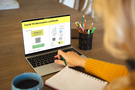 Caucasian woman using laptop with covid vaccination certificate and qr code on screen