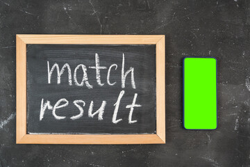 The text of the MATCH RESULT on a chalkboard, a smartphone with a green screen next to it, top view